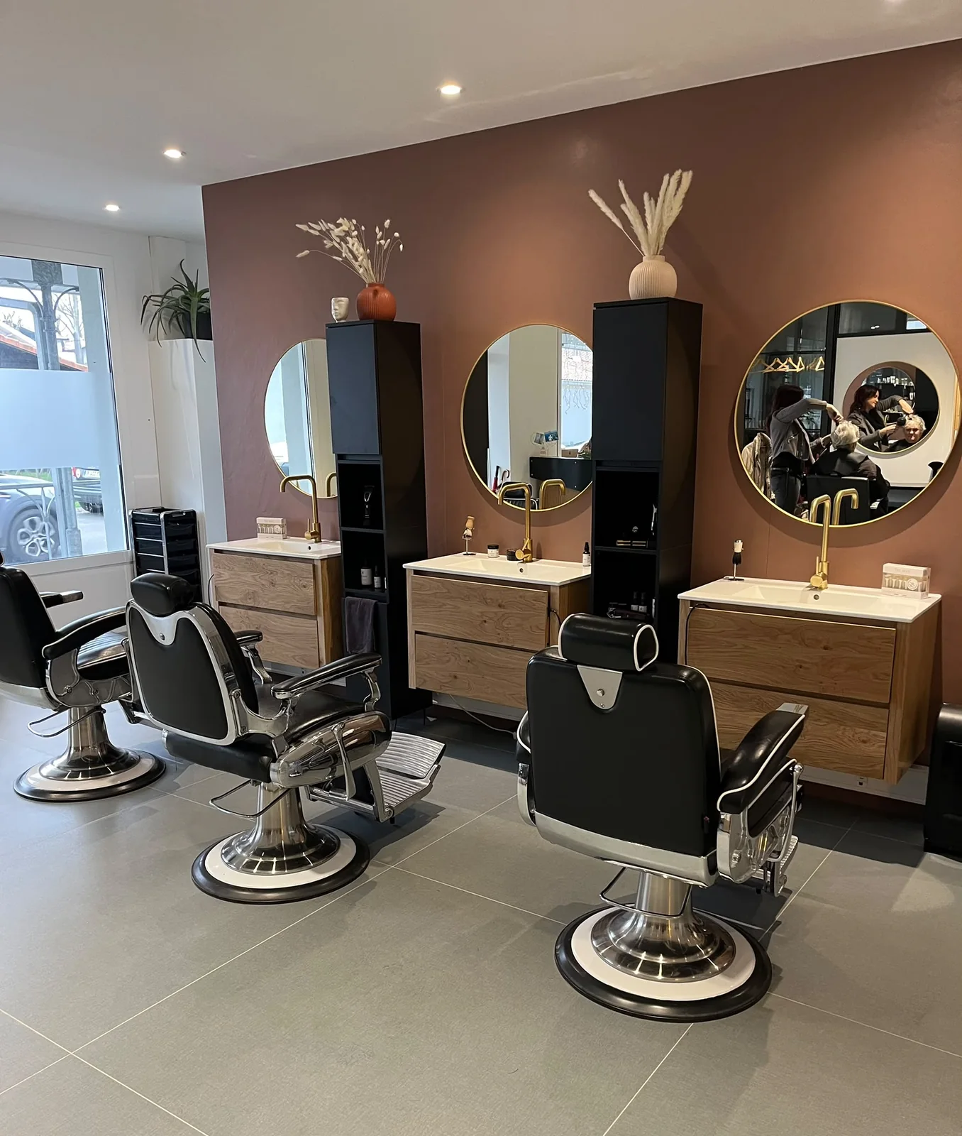 Espace barbier du salon LM Coiffure à Audenge : fauteuils barbier vintage, miroirs ronds dorés et mur terracotta